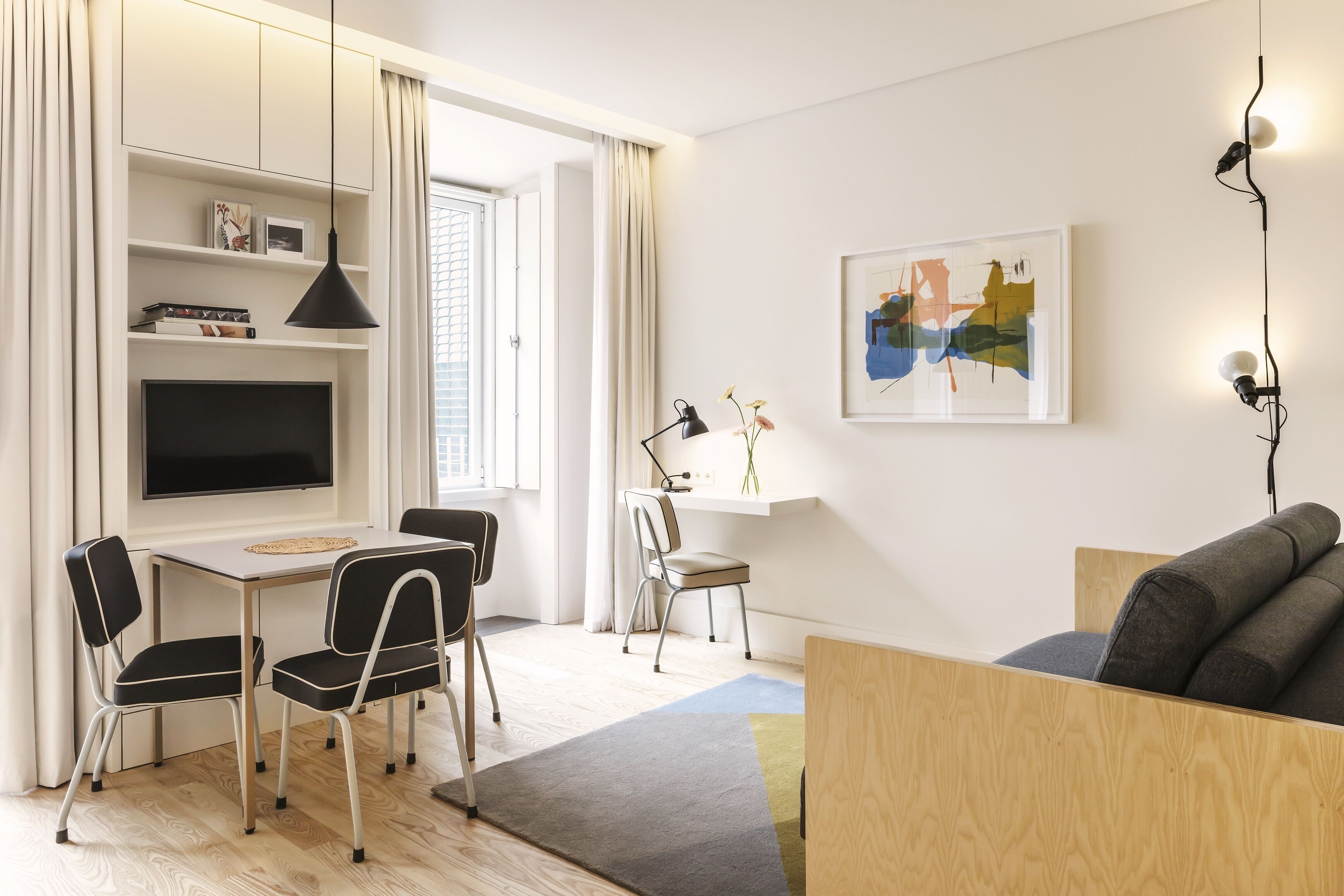 A modern living room with a flat-screen TV, a dining table with chairs, a wooden sofa, and a painting on the wall.