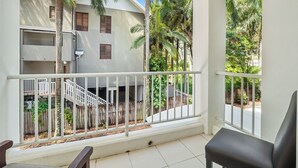A balcony with a white railing, a black chair, and a view of a building with multiple floors and a wooden fence.