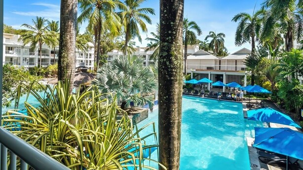 A resort with a clear swimming pool surrounded by palm trees and lounge chairs.