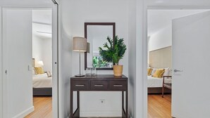 A modern bedroom with a bed, bedside table, lamp, and a potted plant.