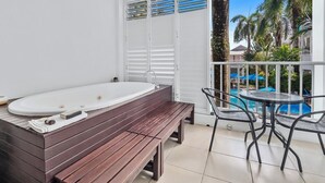 A bathroom with a wooden bench, a bathtub, and a view of a pool and palm trees.