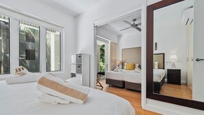 A modern hotel room with a large bed, a sitting area with a sofa and armchairs, a dining table, and a large mirror.