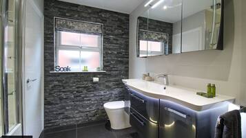 A modern bathroom with a stone wall, a large mirror, a white toilet, and a sink with toiletries.