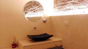 Un baño con un espejo redondo, un lavamanos tipo cuenco negro, un perchero y una pequeña botella de jabón líquido.
