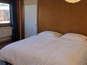 Ein Schlafzimmer mit einem Bett, einem Fenster mit Vorhängen und einer Tür.