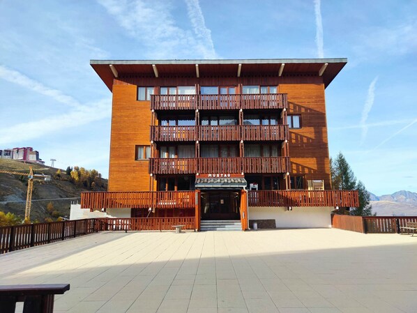 A multi-story wooden building with balconies, a sign reading "MUSTA", and a paved terrace in front.