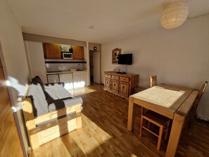Un espacio habitable compacto con kitchenette, un sofá, una mesa de comedor de madera y un televisor.
