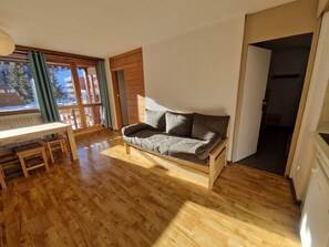 A cozy room with a wooden floor, a built-in sofa, a small wooden table, and a window with curtains.