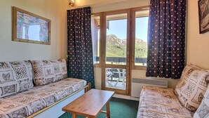 Ein gemütliches Zimmer mit einer Couch, einem Holztisch und Blick auf eine Berglandschaft durch eine Glasdoor.