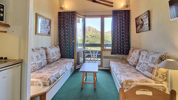 Ein gemütliches Zimmer mit Holzboden, zwei gestreiften Sofas, einem kleinen Tisch und Bergblick durch eine Glastür.