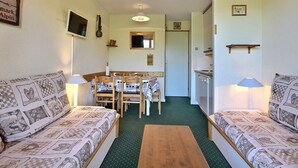 Ein gemütliches Wohnzimmer mit zwei gestreiften Sofas, einem Holztisch, einem Esstisch mit Stühlen, einer Küchenzeile mit Herd und einem an der Wand befestigten Fernseher.