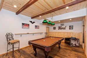 Ein Billardtisch in einem Raum mit Holzbalken an der Decke, eine Billardkeule und ein Billardball.