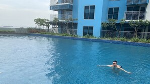 Une piscine à l’eau cristalline, entourée d’un bâtiment moderne doté de balcons et offrant une vue sur la mer.