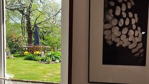 A room with a door leading to a garden, a framed artwork on the wall, and a small table with a lamp. - Country house on the edge of a forest with landscaped garden. (Billio)
