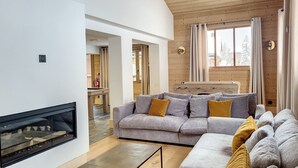 Ein modernes Wohnzimmer mit Kamin, grauen Sofas mit gelben Kissen, Holzwänden und einem großen Fenster mit Vorhängen.