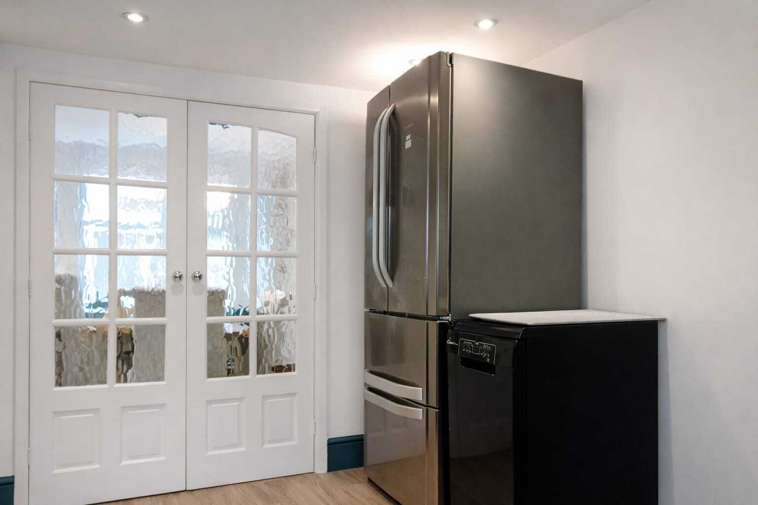 A kitchen with a stainless steel refrigerator, a black dishwasher, and a white door with frosted glass panels.