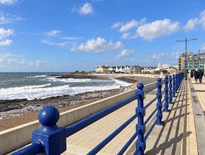 A coastal promenade with a blue railing, rocky beach, and buildings in the background. - Modern, light-filled townhouse with a king bed, spacious living room with an electric fireplace, fully equipped kitchen, dedicated workspace, and free on-site parking for one car. Enjoy a private outdoor patio . (Bridgend County Borough)