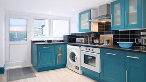 A modern kitchen with teal cabinets, a washing machine, an oven, and a microwave. - Ty Hapus is a modern, spacious townhouse featuring a King bed, fully equipped kitchen, and a private fenced backyard with a fire pit. Located in a highly walkable neighborhood near historic sites, vibrant dining, and beautiful beaches, room for six (Bridgend County Borough)