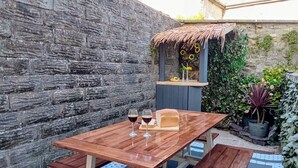 A wooden table with benches in a garden area with a stone wall and potted plants. - Ty Hapus is a modern, spacious townhouse featuring a King bed, fully equipped kitchen, and a private fenced backyard with a fire pit. Located in a highly walkable neighborhood near historic sites, vibrant dining, and beautiful beaches, room for six (Bridgend County Borough)