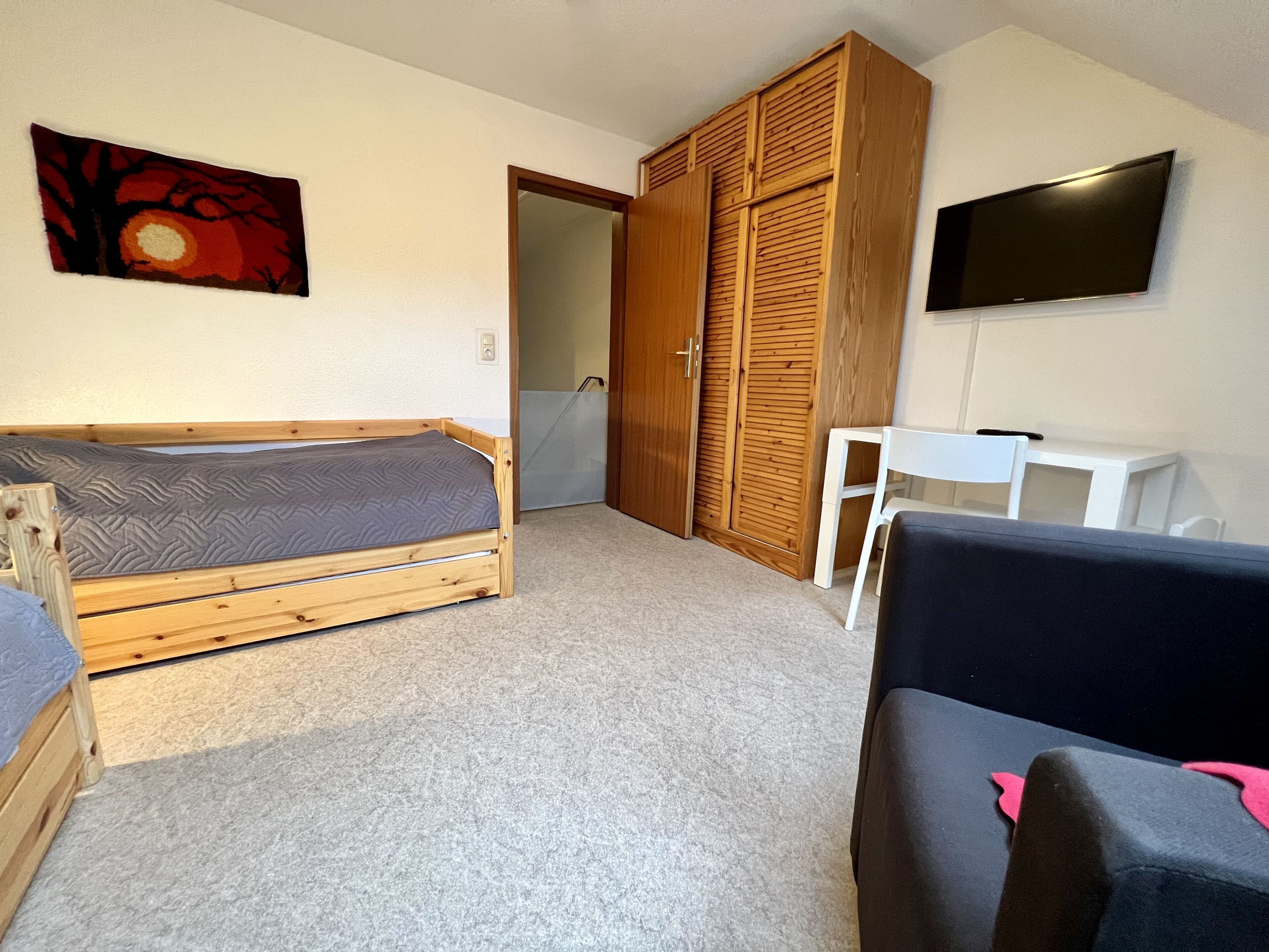 Quarto com cama de madeira, guarda-roupa, televisão e uma pequena mesa.