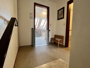 A hallway with a glass door leading to a room, a wooden bench, and a framed picture on the wall.