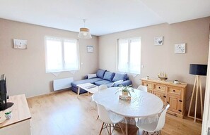 A cozy living room with a sofa, a dining table with chairs, and a TV. - 3-star apartment 63 m2 (Cabourg)