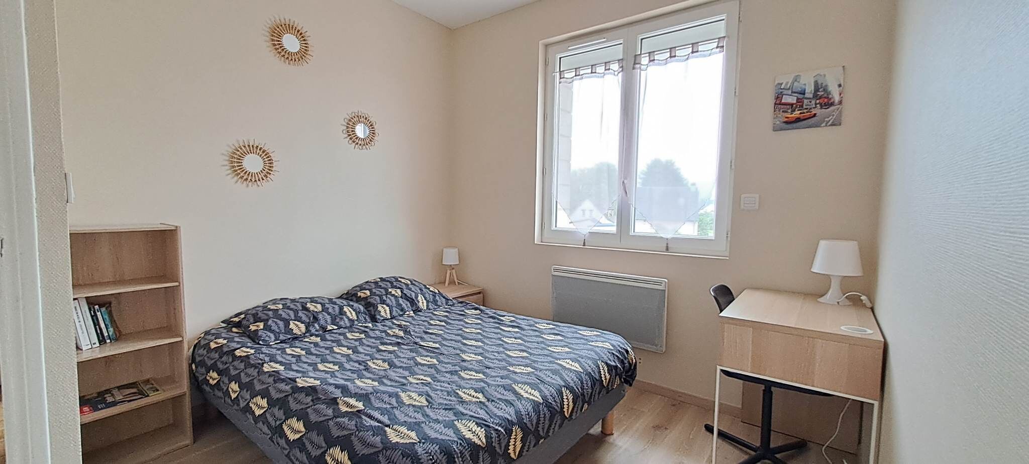 A bedroom with a bed, a desk, a radiator, and a window.