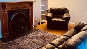 Una sala de estar con chimenea, un sofá de cuero negro, un ventilador de techo azul y una estantería.