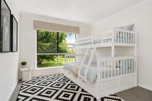 A room with a bunk bed, a window with a view of greenery, a patterned rug, and framed artwork on the wall. - La Maison Ver La Mer by Ready Set Stay - Big & Beautiful Backyard (Rye)