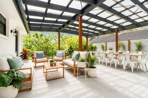 Een terras buiten, met een overdekte zithoek, tafels en potplanten.