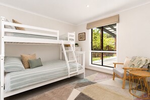 Een slaapkamer met een stapelbed, raam, stoel en een klein tafeltje.
