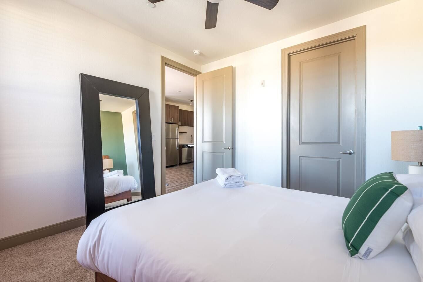 Habitación de hotel con cama, espejo, puerta y vista hacia la cocina.