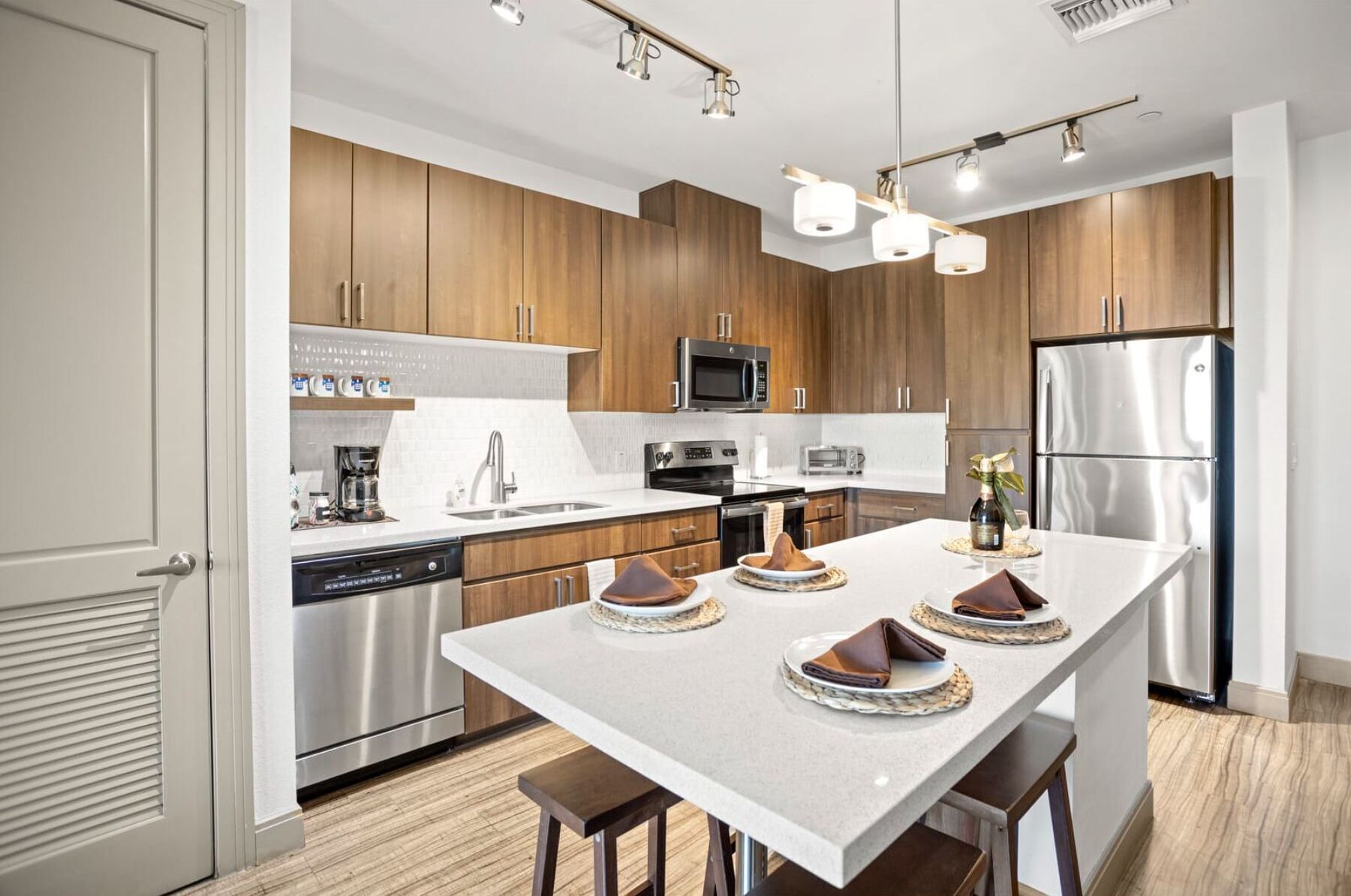 A modern kitchen with wooden cabinets, stainless steel appliances, and a central island with stools.