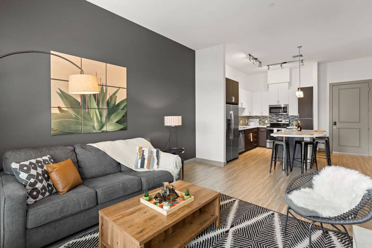 A modern living room with a grey sofa, a wooden coffee table, and a black and white patterned rug.