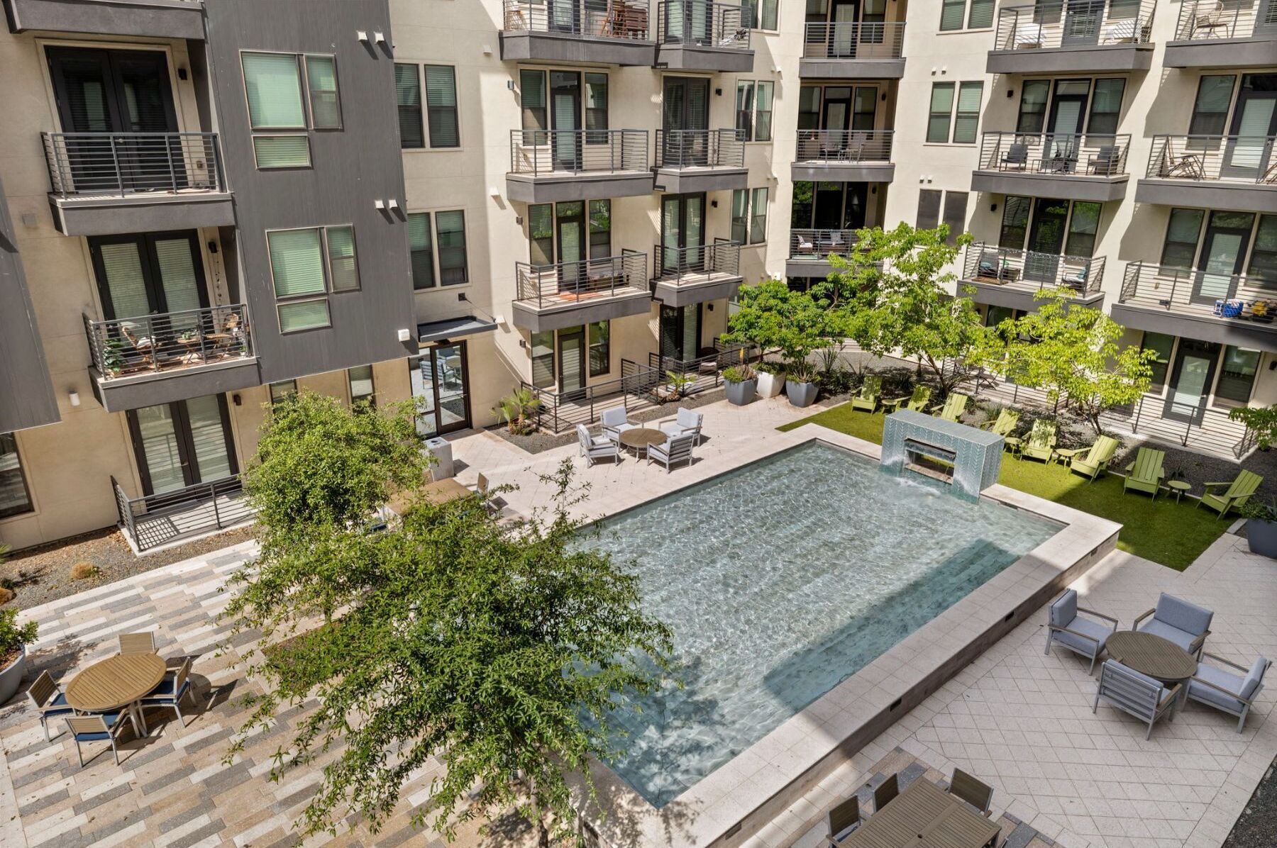 A modern apartment complex with a central courtyard featuring a swimming pool, outdoor seating, and balconies.