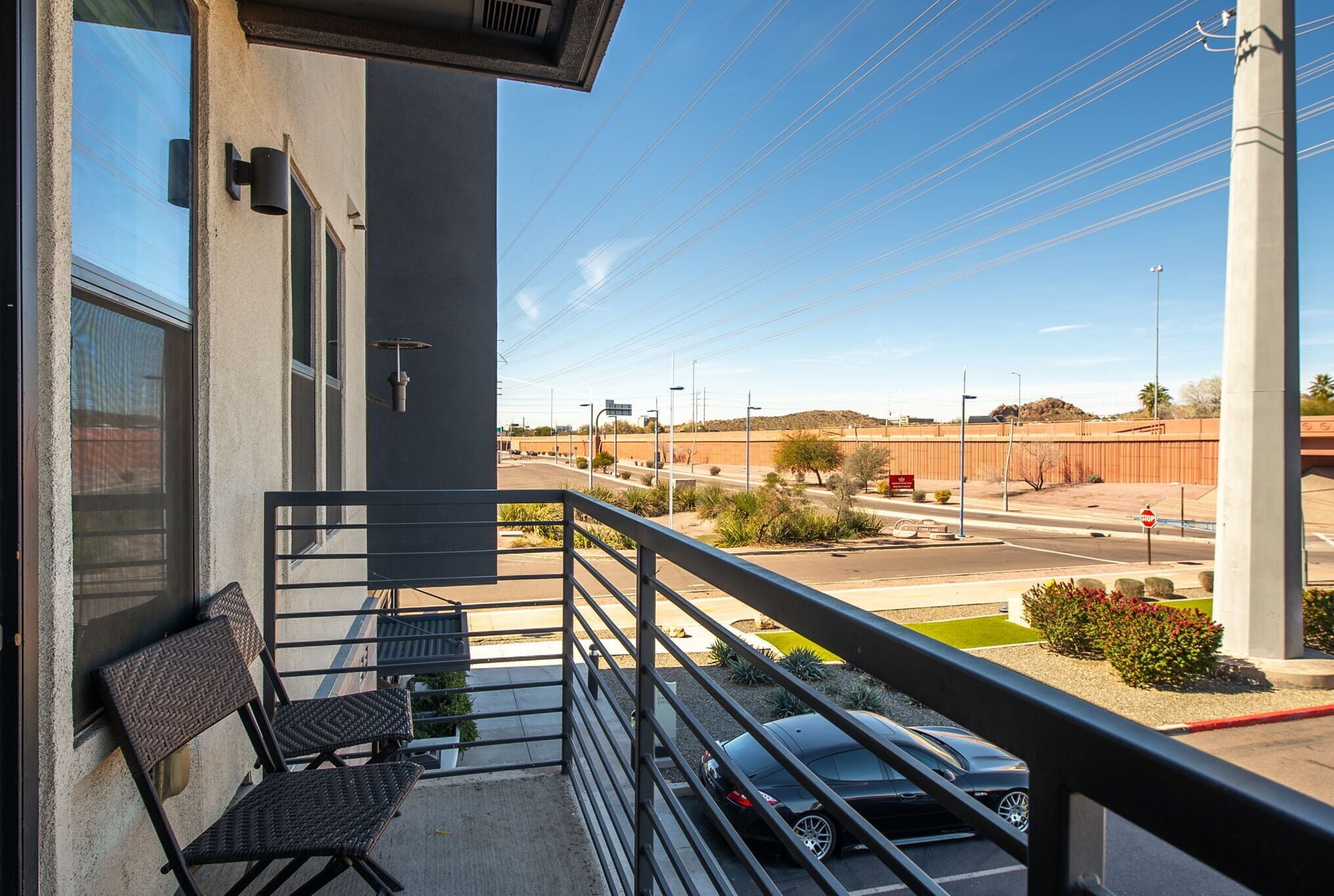 A balcony with two wicker chairs, a view of a parking lot, and a street with a stop sign.