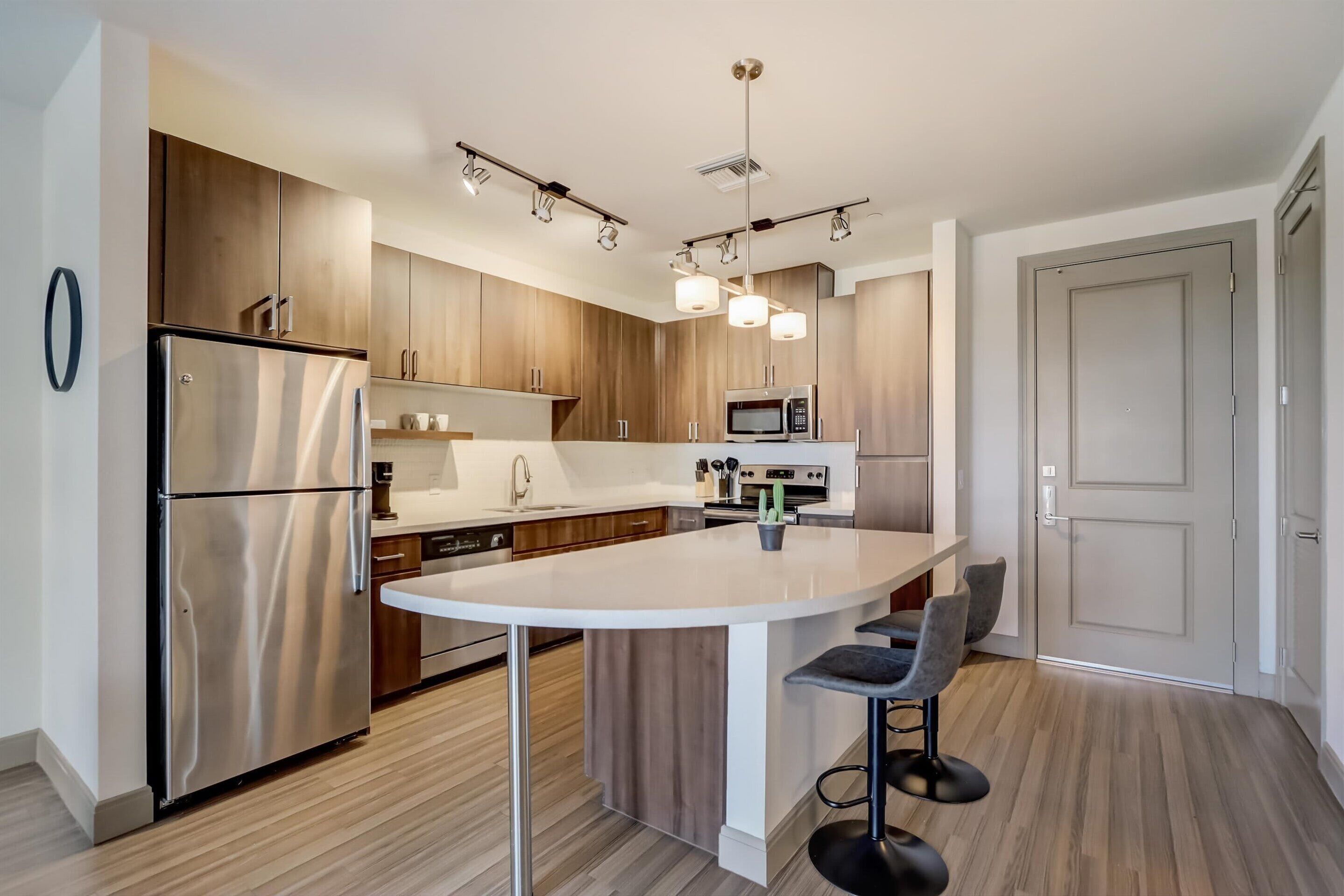 Cocina moderna con una isla central, electrodomésticos de acero inoxidable, armarios de madera y una zona de asientos con taburetes de bar.