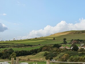 A rural landscape with rolling hills, a few scattered houses, and a clear sky. - Cliff Barn (Bridport)