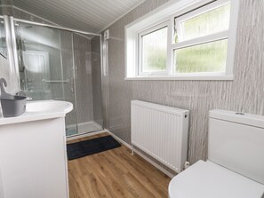 A bathroom with a shower, toilet, sink, and a window with a view. - Cliff Barn (Bridport)