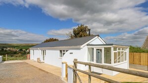 A white cottage with a fenced yard, a covered porch, and a view of the countryside. - Cliff Barn (Bridport)