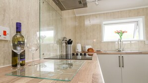 A modern kitchen with a glass-top island, stainless steel appliances, and a window with a view. - Cliff Barn (Bridport)