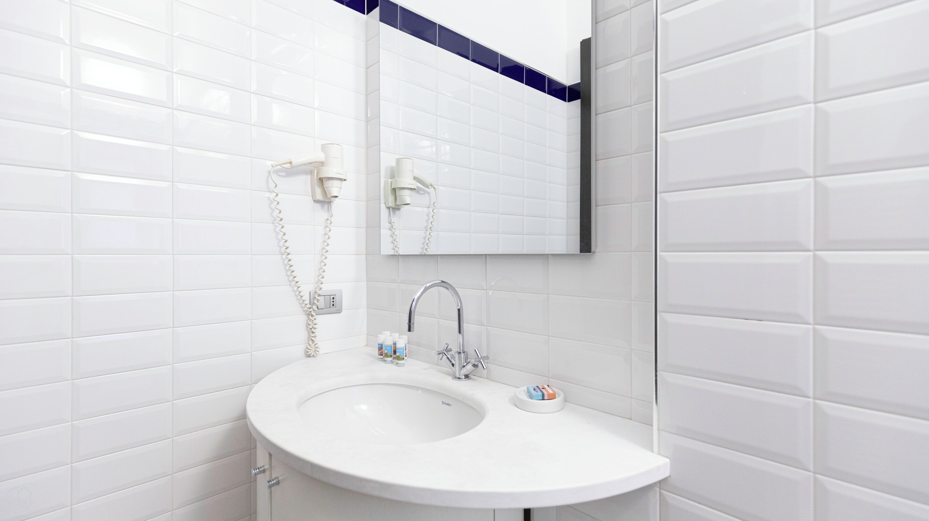 A modern bathroom with white tiled walls, a white sink with a single faucet, and a mirror above the sink.