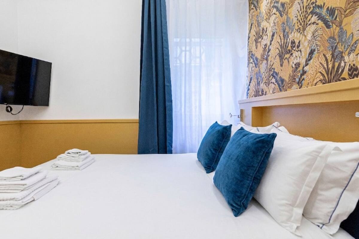 A hotel room with a bed, pillows, a TV, and a window with curtains.