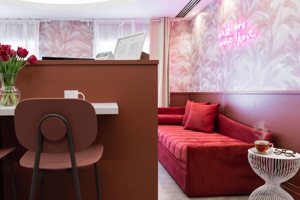 A modern room with a red sofa, a small white side table with a cup and glasses, and a vase with red flowers on a table.