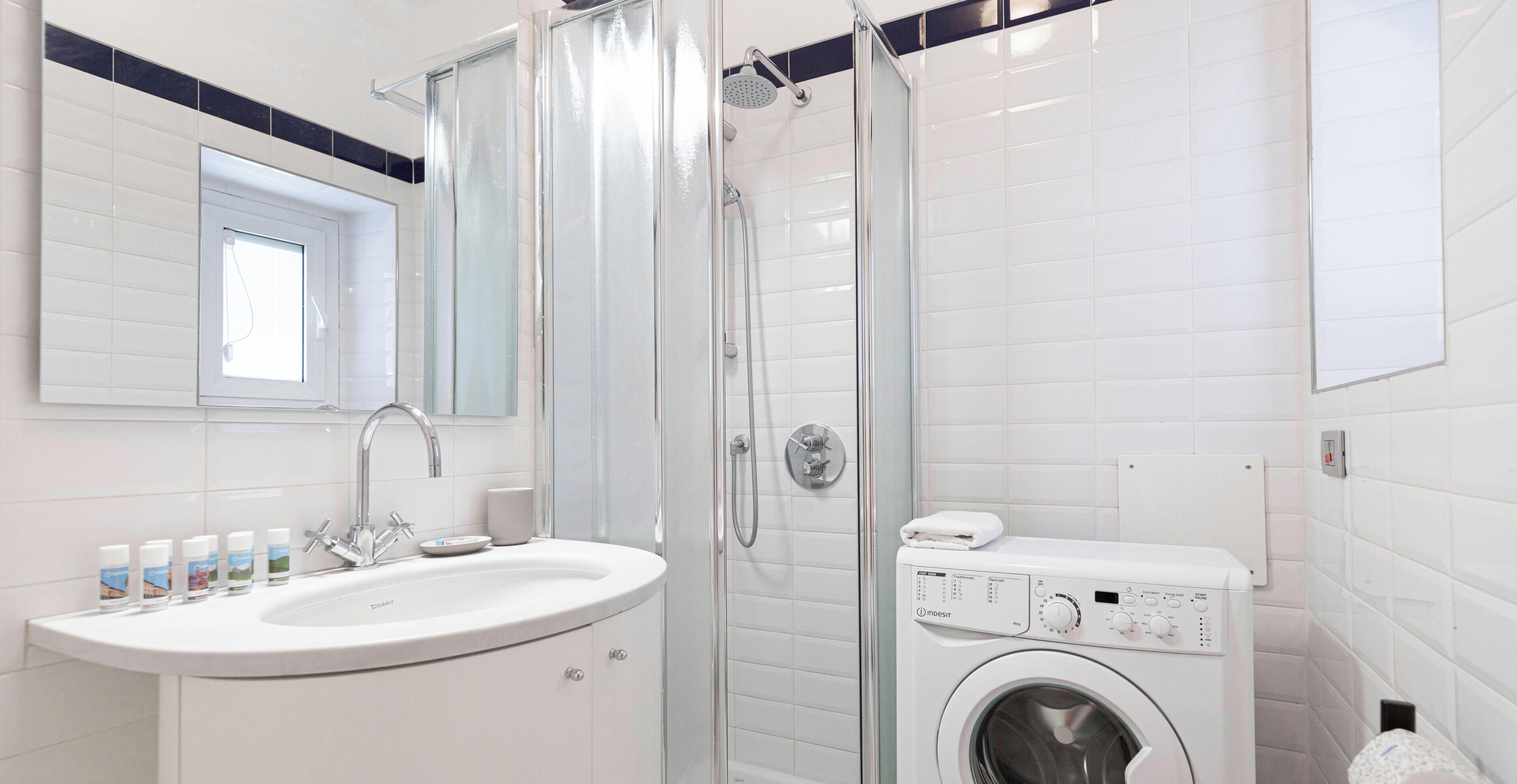 A modern bathroom with a glass-enclosed shower, a sink with a mirror, and a built-in washing machine.