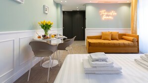 A hotel room with a bed, a table with breakfast items, two chairs, a sofa, and a neon sign. - Italianway - Corso Venezia 7 (Milan)