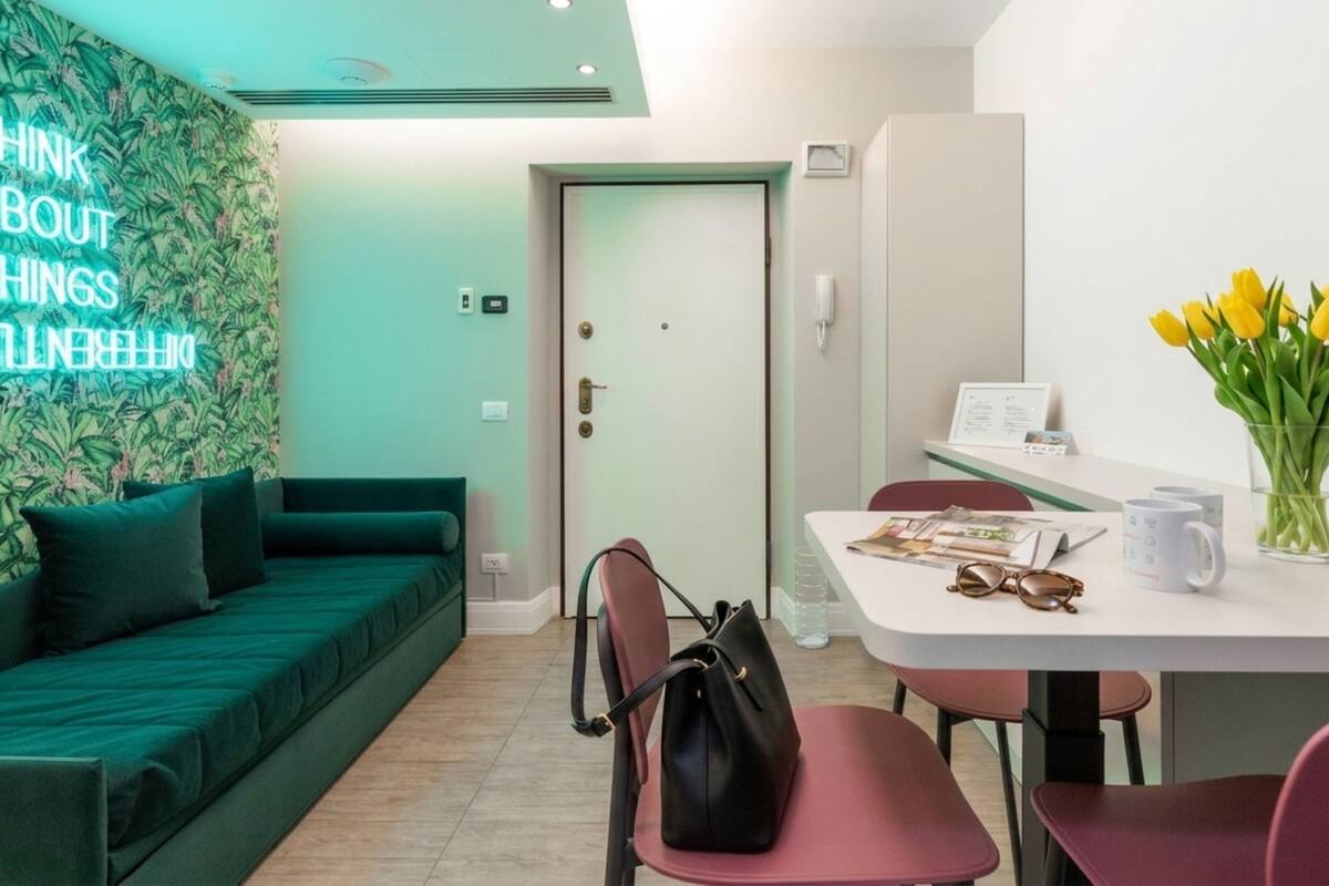 A modern room with a teal sofa, a dining table with chairs, a black handbag, and a vase of yellow tulips.