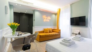 A hotel room with a bed, a sofa, a TV, a table with a chair, and a neon sign on the wall. - Italianway - Corso Venezia 7 (Milan)