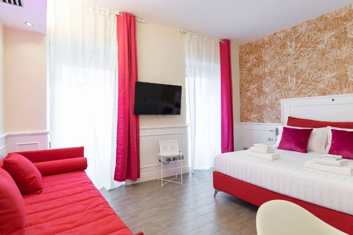 A hotel room with a bed, a sofa, a TV, and a fireplace.