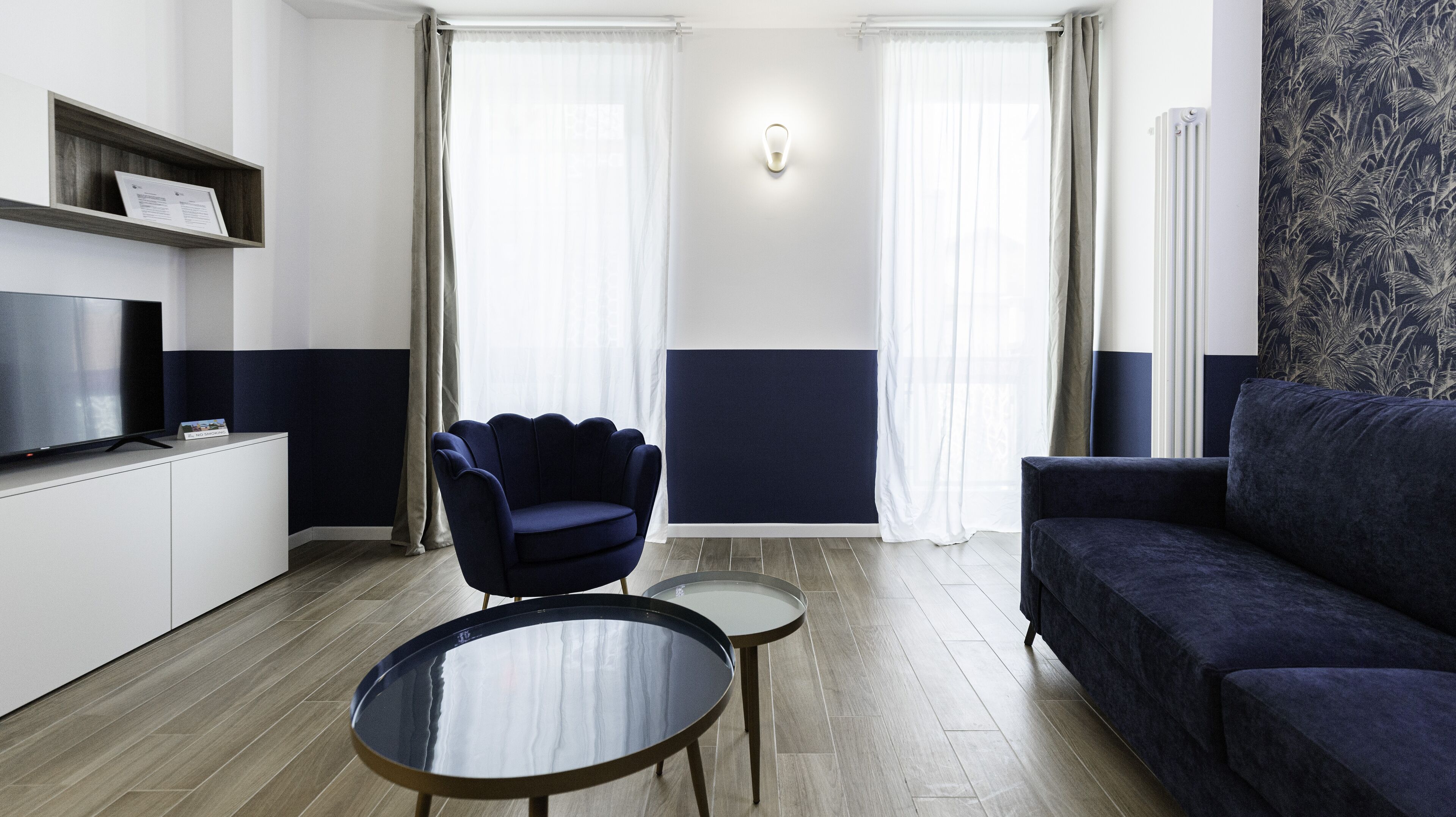 A modern living room with a flat-screen TV, a dark blue sofa, a matching armchair, and a small round table.